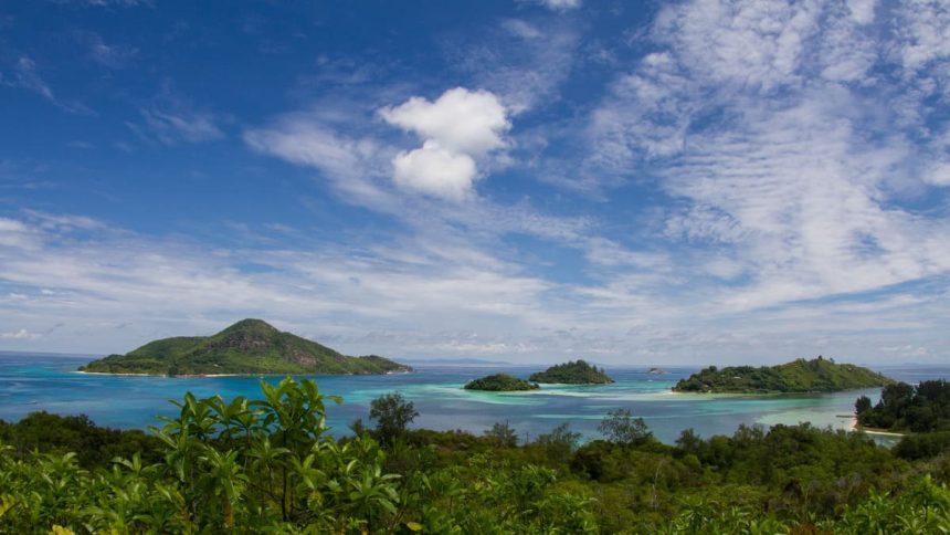 Petites îles boisées entourées d'un lagon turquoise aux Seychelles, vues depuis la végétation d'un rivage