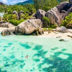 Vue aérienne d'une côte des Seychelles : blocs de granit, cocotiers et lagon turquoise, avec un kayak transparent